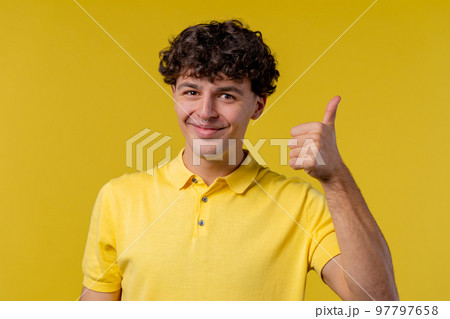 Positive curly man makes hand sign like, thumbs up gesture. Happy student guy in yellow, correct 97797658