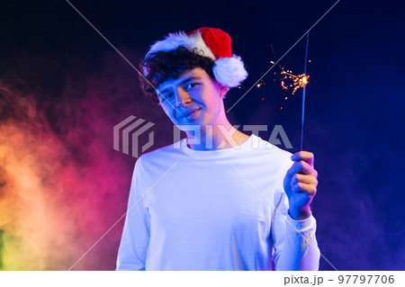 Young man in Santa hat with bengal sparkler fire under neon light. New year or Christmas party Young man in Santa hat with bengal sparkler fire under neon light. New year or Christmas party 97797706