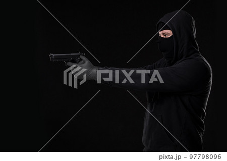 The robber in a mask with a gun pointed to the side on a black background The robber in a mask with a gun pointed to the side on a black background 97798096