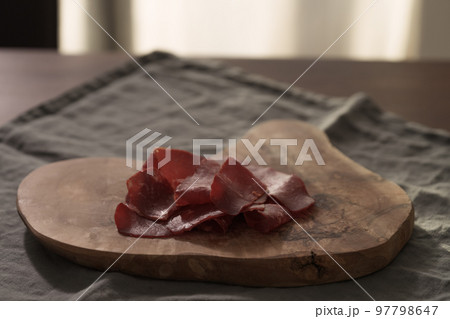 Dried pastrami slices on a wooden board with natural light Dried pastrami slices on a wooden board with natural light 97798647