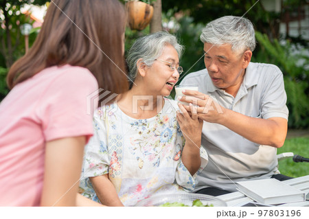 Happy Asian family enjoy lunch together in backyard. Husband feeding milk wife. Concept of a happy family together. Happy Asian family enjoy lunch together in backyard. Husband feeding milk wife. Concept of a happy family together. 97803196