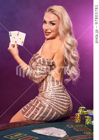 Blonde woman with a perfect hairstyle and bright make-up is posing with playing cards in her hands. Casino, poker. 97803781