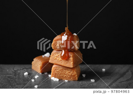 Pouring delicious salted caramel on candies against black background 97804963
