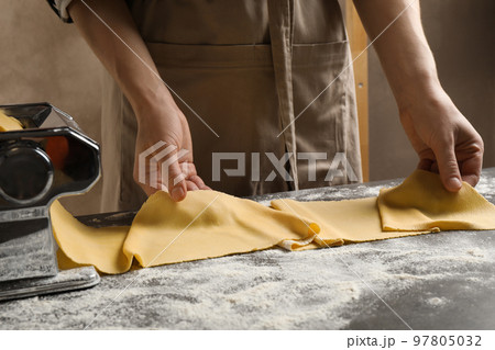 Woman preparing dough with pasta maker machine at grey table, closeup Woman preparing dough with pasta maker machine at grey table, closeup 97805032