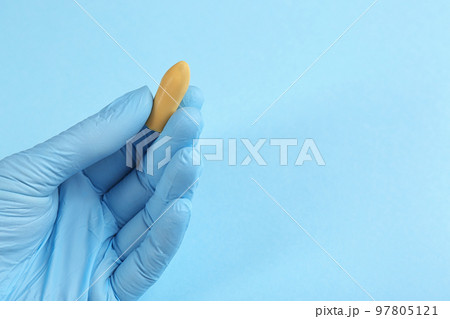 Closeup view of woman holding suppository on light blue background, space for text. Hemorrhoid treatment 97805121