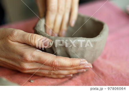 Women's hands knead the clay and sculpt a cup or bowl from it. The process of manufacturing a ceramic product,close up Women's hands knead the clay and sculpt a cup or bowl from it. The process of manufacturing a ceramic product,close up 97806064