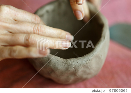 Women's hands knead the clay and sculpt a cup or bowl from it. The process of manufacturing a ceramic product,close up Women's hands knead the clay and sculpt a cup or bowl from it. The process of manufacturing a ceramic product,close up 97806065