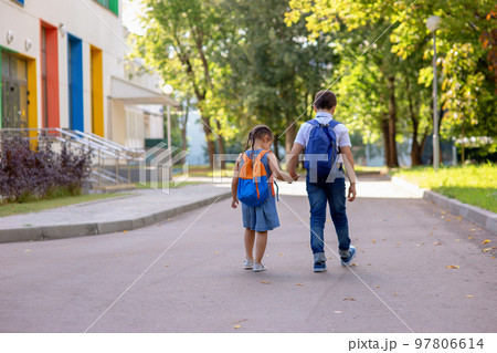 a little girl and a boy in a white shirt with backpacks go on the way to school. 97806614