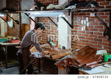 Asian craftsman in apron working with leather in workshop 97808530