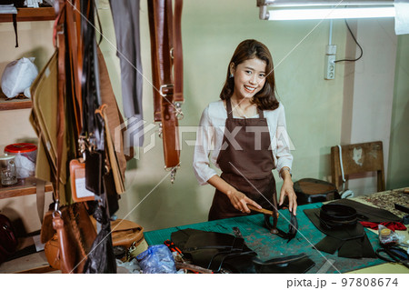 Smiling craftswoman using a hammer smoothing the zipper edge 97808674