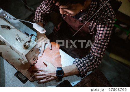 man tailor sewing leather using sewing machine with table lamp 97808766
