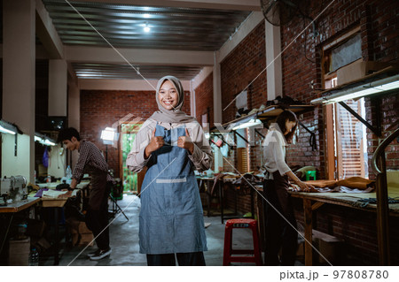 Smiling female leather craftsman with two thumbs standing in studio Smiling female leather craftsman with two thumbs standing in studio 97808780