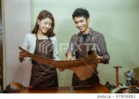 Young asian tailor couple holding leather pattern together at work Young asian tailor couple holding leather pattern together at work 97808883