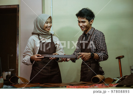 craftsman and craftswoman wearing a hijab make a leather belt 97808893