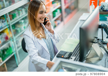 Attractive female pharmacist working in while making phone call Attractive female pharmacist working in while making phone call 97808904