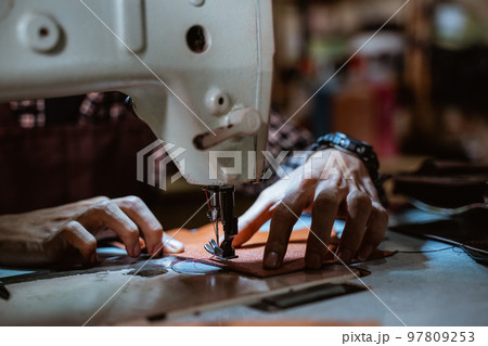 Close up of tailor's hand sewing leather using sewing machine Close up of tailor's hand sewing leather using sewing machine 97809253
