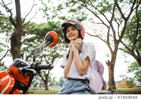 Student girl carrying school bag tightens helmet strap on motorbike Student girl carrying school bag tightens helmet strap on motorbike 97809688