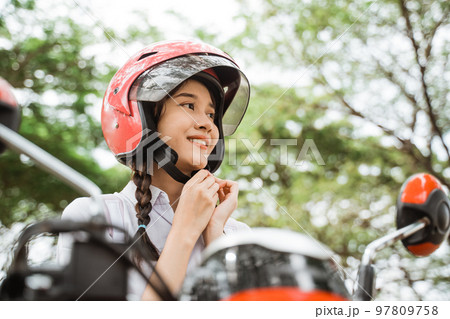 Close up of student girl tightening helmet strap on motorbike Close up of student girl tightening helmet strap on motorbike 97809758