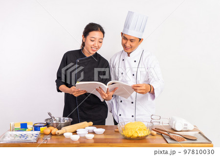 male and female chefs using cookbooks standing near table 97810030