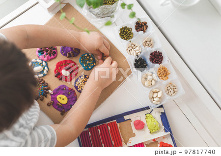 Baby boy creating plasticine diy figure with decorate dried beans element early development top view Baby boy creating plasticine diy figure with decorate dried beans element early development top view 97817740