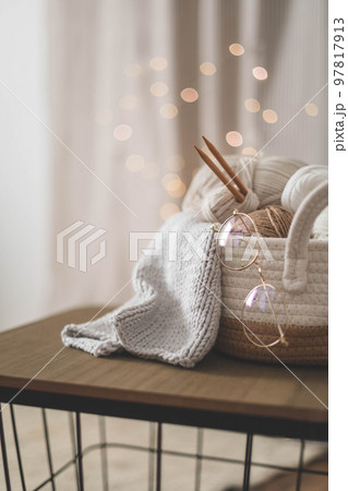 Cozy homely atmosphere. Female hobby knitting. Yarn in neutral shades in a soft basket of white 97817913