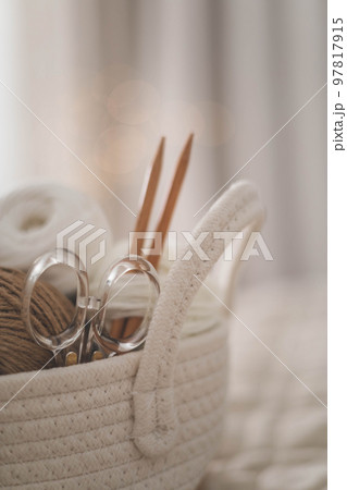 Cozy homely atmosphere. Female hobby knitting. Yarn in neutral shades in a soft basket of white Cozy homely atmosphere. Female hobby knitting. Yarn in neutral shades in a soft basket of white 97817915