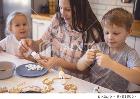 Mom and kids make snowmen from marshmallows. They drink cocoa and get ready for Christmas. Christmas home concept. Mom and kids make snowmen from marshmallows. They drink cocoa and get ready for Christmas. Christmas home concept. 97818057