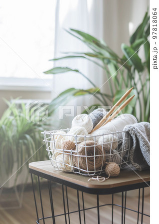 Cozy homely atmosphere. Female hobby knitting. Yarn in neutral colors in a white iron wire basket. 97818064