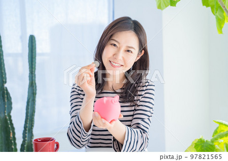 明るいリビングで貯金箱に貯金する女性 97821565