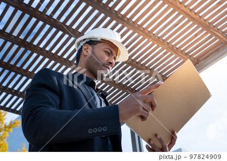 African American businessman manager with construction helmet reviewing blueprints for a project. 97824909