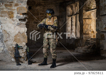 A woman in an army uniform holds a firearm in an abandoned building. 97825611