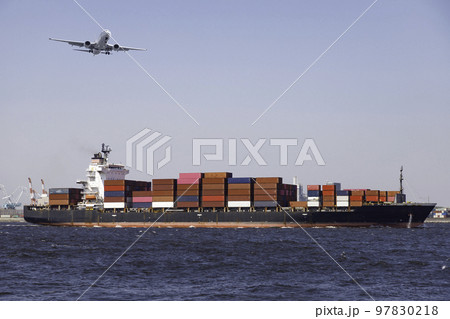 青空を背景に港を航行するコンテナ船と上を通過する飛行機 97830218
