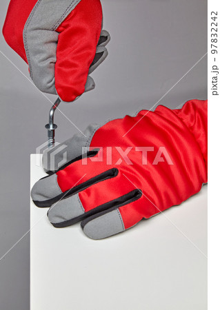 Furniture assembler in red gloves is screwing in a screw with a hex wrench Furniture assembler in red gloves is screwing in a screw with a hex wrench 97832242