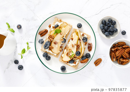 Crispbread with cream cheese, sweet pears, blueberry and pecan nuts. Top view 97835877
