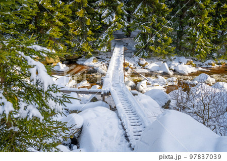 Small wooden footbridge covered by snow over icy mountain river in wintertime. 97837039