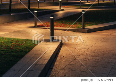 Row Of Outdoor Landscape Hard Paving Light. Lighting element on the green lawn along the footpath. Modern lighting system in landscape design. Row Of Outdoor Landscape Hard Paving Light. Lighting element on the green lawn along the footpath. Modern lighting system in landscape design. 97837494