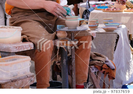 Potter uses a tool to cover clay cup with paint. Pottery and craftsmanship concept. Potter uses a tool to cover clay cup with paint. Pottery and craftsmanship concept. 97837659
