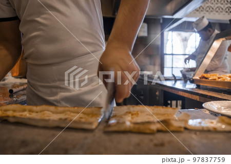 Midsection of male chef cutting Turkish cheese pide into slices on table in commercial kitchen at restaurant Midsection of male chef cutting Turkish cheese pide into slices on table in commercial kitchen at restaurant 97837759