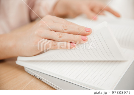 Close up of a woman's hands writing in a notepad placed on a wooden table, home office and work concept, plans and thoughts Close up of a woman's hands writing in a notepad placed on a wooden table, home office and work concept, plans and thoughts 97838975