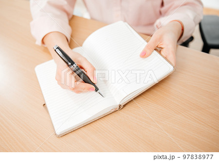 Close up of a woman's hands writing in a notepad placed on a wooden table, home office and work concept, plans and forecasts 97838977