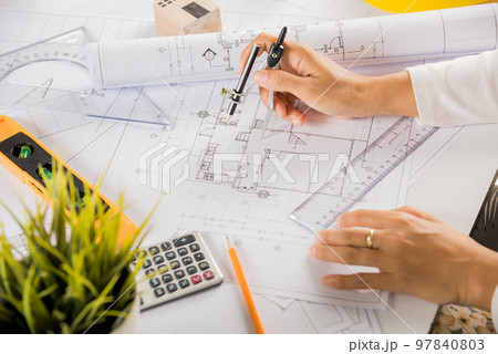 Architectural project workplace. Architect drawing with divider compass on house plan blueprint paper for repair tools on table desk at architecture office, Engineer sketching construction project Architectural project workplace. Architect drawing with divider compass on house plan blueprint paper for repair tools on table desk at architecture office, Engineer sketching construction project 97840803