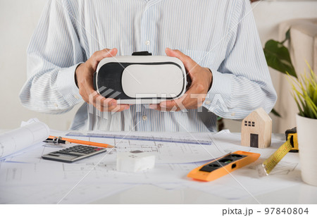 Architectural building design holding 3D VR glasses and construction plans with blueprints paper project plans, designing man edit building or architecture, technology industry, Architect workplace 97840804