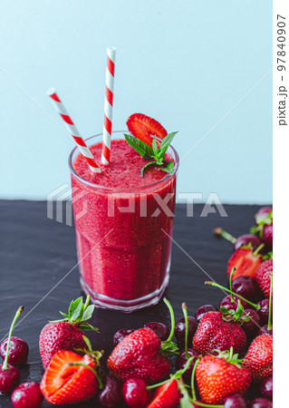 Fresh berry juice or smoothie with straw with fresh strawberries and cherries on blue background. 97840907