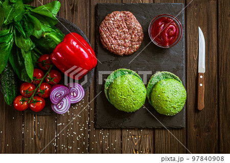 Top down view of process of making burger with vegetables, green buns and artificial meat on board 97840908