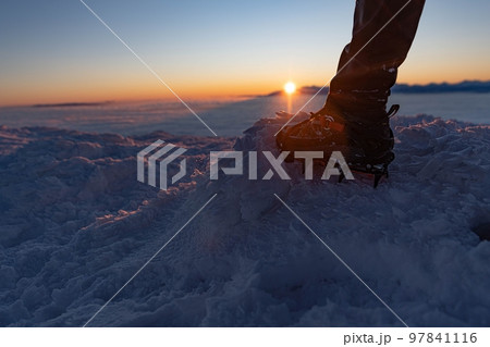 Man climbs a mountain peak in winter during sunrise. A shoe with spikes on - crampons.  97841116