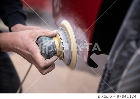 Painter is repairing the damage on the bumper of the red car 97841124