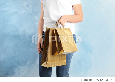 Woman with gold shopping paper bags on light blue background, closeup 97841817
