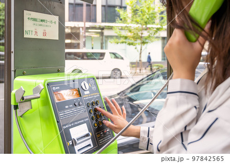 携帯電話の通信障害で公衆電話を使う若い女性のイメージカット 97842565