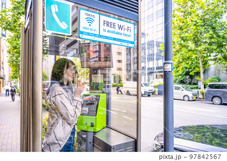 携帯電話の通信障害で公衆電話を使う若い女性 携帯電話の通信障害で公衆電話を使う若い女性 97842567