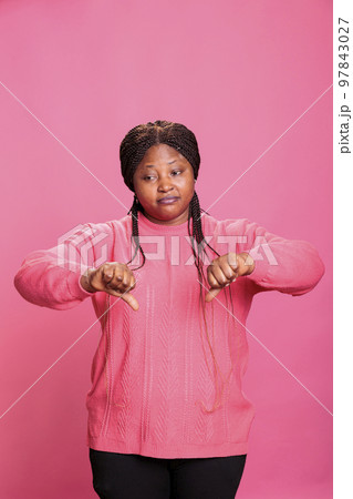 Dissatisfied unhappy woman showing dislike gesture on camera in studio, gesturing disagreement sign with fingers. Displeased person expressing disapproval and disappointment, doing dislike symbol. 97843027